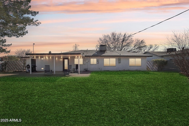 back house at dusk featuring a patio area and a lawn