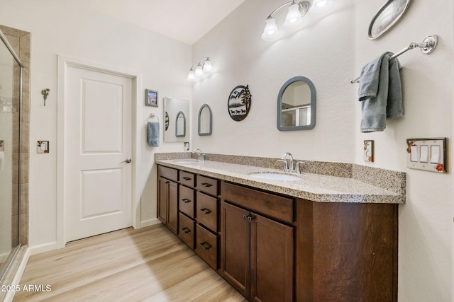 bathroom with wood finished floors, a tile shower, double vanity, and baseboards