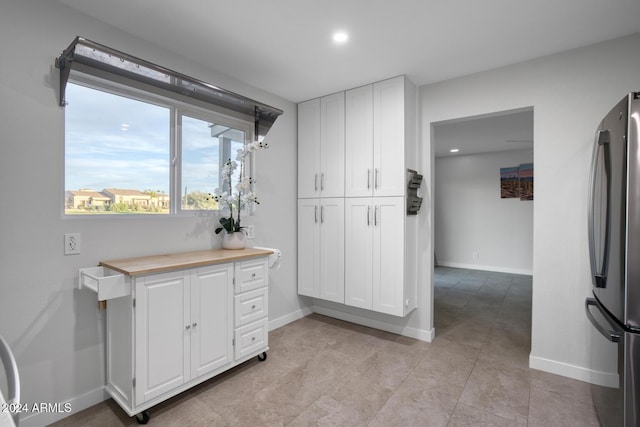 kitchen with butcher block counters, white cabinetry, and stainless steel refrigerator