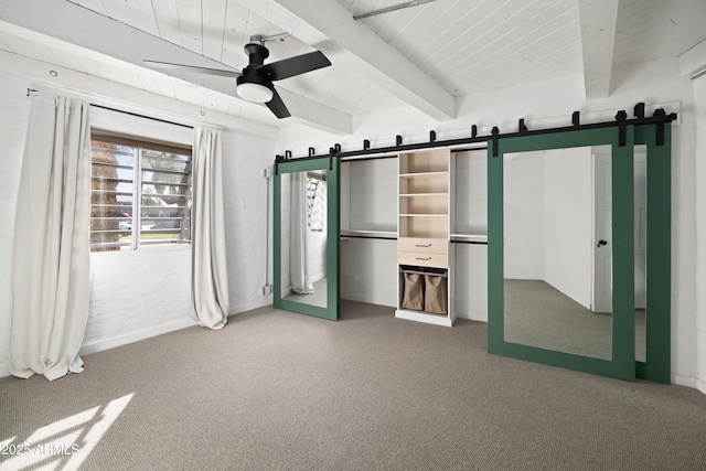 unfurnished bedroom with carpet, beam ceiling, a barn door, and ceiling fan