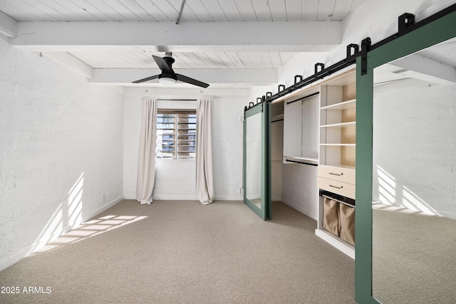 unfurnished bedroom featuring carpet flooring, a barn door, ceiling fan, and beam ceiling