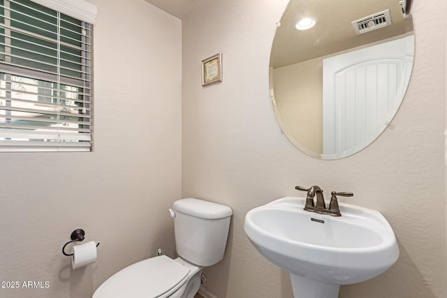 half bathroom featuring toilet, visible vents, and a sink