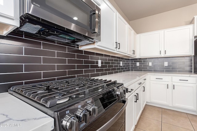 kitchen with light stone counters, light tile patterned floors, black range with gas cooktop, white cabinetry, and stainless steel microwave