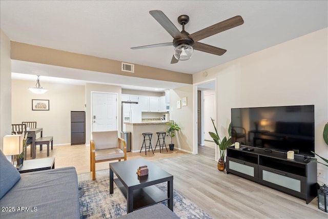 living area with a ceiling fan, light wood-style floors, visible vents, and baseboards