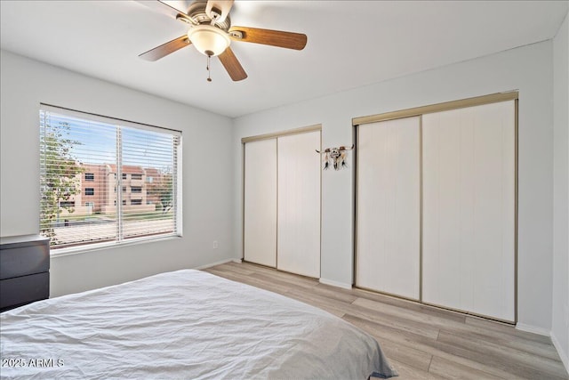 bedroom with baseboards, multiple closets, ceiling fan, and wood finished floors