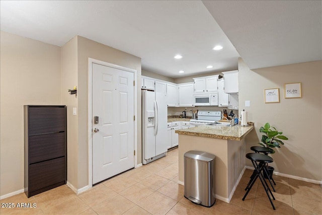 kitchen featuring recessed lighting, white appliances, a kitchen bar, a peninsula, and white cabinets