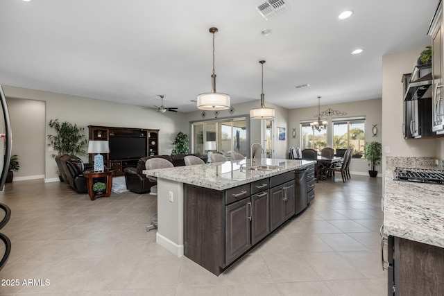 kitchen featuring sink, hanging light fixtures, a kitchen island with sink, light stone countertops, and dark brown cabinets