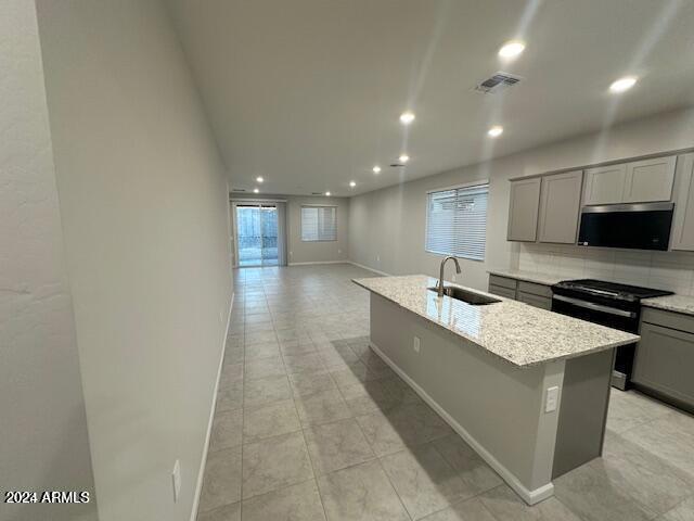 kitchen featuring light stone countertops, appliances with stainless steel finishes, sink, a center island with sink, and gray cabinets