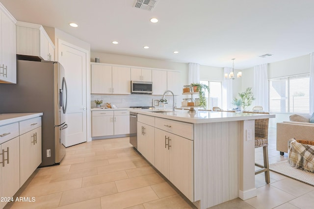 kitchen featuring a notable chandelier, a center island with sink, decorative backsplash, appliances with stainless steel finishes, and decorative light fixtures