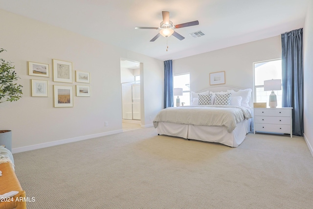 bedroom with ceiling fan, light carpet, and ensuite bath