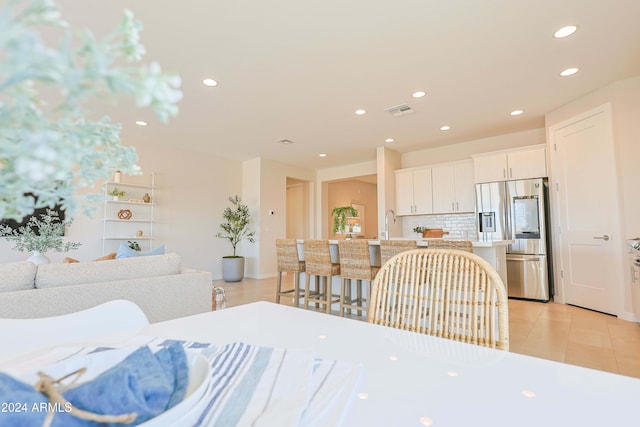 kitchen featuring a breakfast bar, stainless steel fridge, light tile patterned floors, tasteful backsplash, and white cabinetry