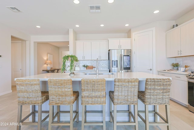 kitchen with backsplash, stainless steel appliances, sink, a breakfast bar area, and an island with sink