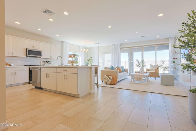 kitchen with appliances with stainless steel finishes, backsplash, an inviting chandelier, hanging light fixtures, and an island with sink