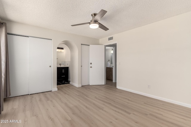 12529 N 83rd Ln, Peoria, AZ 85381 - unfurnished bedroom with two closets, light wood-style flooring, arched walkways, a textured ceiling, and connected bathroom