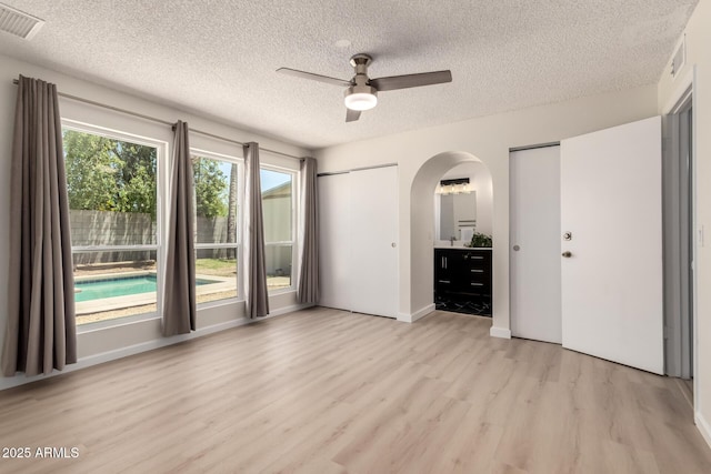 12529 N 83rd Ln, Peoria, AZ 85381 - unfurnished bedroom featuring two closets, arched walkways, light wood-style flooring, a textured ceiling, and ceiling fan