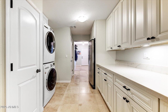 clothes washing area with cabinets, a textured ceiling, and stacked washing maching and dryer