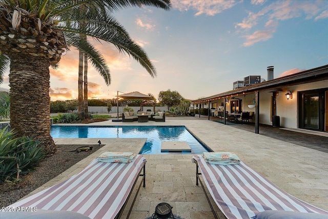 pool at dusk with cooling unit, outdoor lounge area, and a patio area