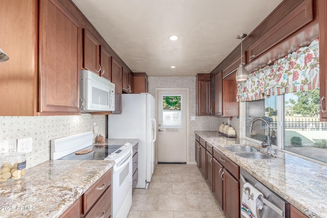 kitchen with decorative light fixtures, light stone counters, white appliances, and sink