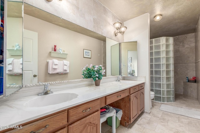 bathroom featuring vanity, toilet, a tile shower, and a textured ceiling