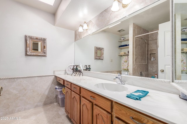 bathroom with vanity, a skylight, tile patterned flooring, tile walls, and a tile shower