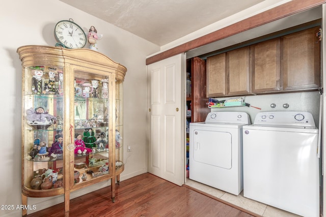 clothes washing area featuring hardwood / wood-style flooring, cabinets, and independent washer and dryer