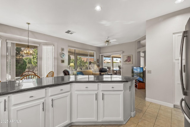 kitchen with white cabinetry, hanging light fixtures, light tile patterned floors, dark stone countertops, and ceiling fan with notable chandelier