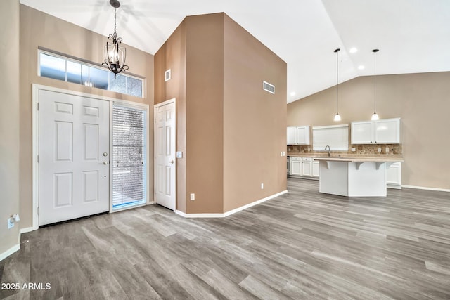 entryway featuring light wood-type flooring, sink, high vaulted ceiling, and a chandelier