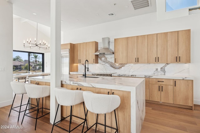 kitchen with sink, wall chimney range hood, an inviting chandelier, light hardwood / wood-style flooring, and pendant lighting