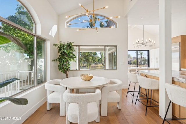 dining space with high vaulted ceiling, a notable chandelier, and light wood-type flooring