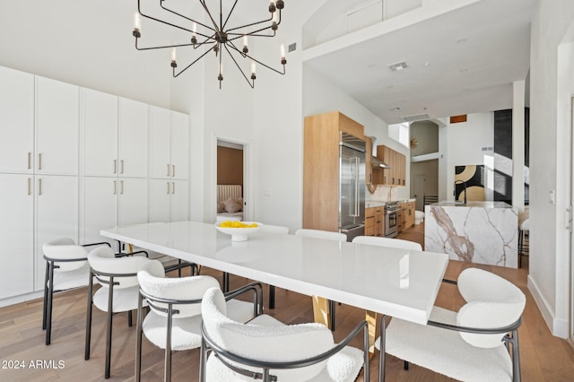 dining room featuring light hardwood / wood-style flooring, a towering ceiling, and a chandelier