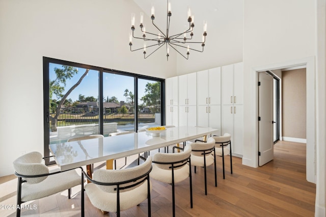 dining area featuring light hardwood / wood-style flooring, a towering ceiling, and a chandelier