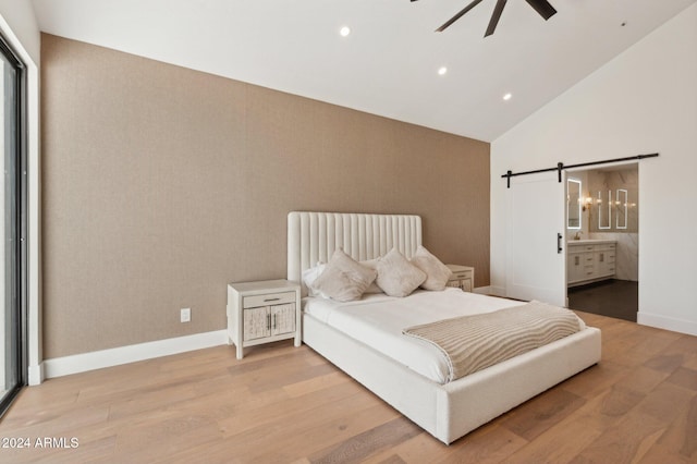 bedroom featuring a barn door, light hardwood / wood-style flooring, ceiling fan, and connected bathroom