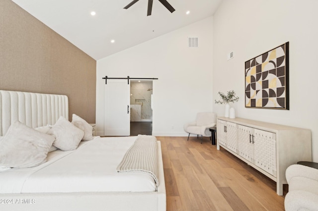 bedroom featuring ceiling fan, a barn door, light wood-type flooring, and high vaulted ceiling