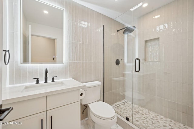 bathroom with a shower with door, vanity, tile walls, and toilet