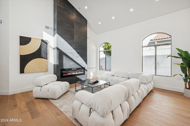 living room featuring high vaulted ceiling, a tiled fireplace, a wealth of natural light, and light hardwood / wood-style flooring