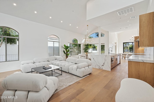 living room featuring sink, high vaulted ceiling, light wood-type flooring, and an inviting chandelier