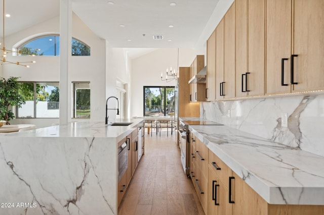 kitchen featuring stainless steel electric range oven, a large island with sink, light brown cabinetry, and light hardwood / wood-style flooring