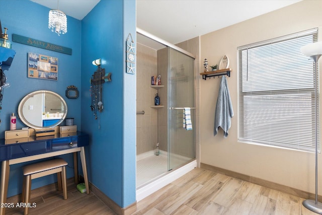 bathroom with an inviting chandelier, a stall shower, baseboards, and wood finished floors