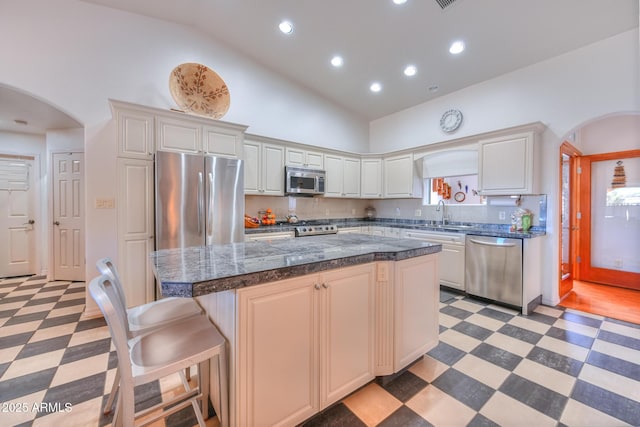 kitchen with tile patterned floors, high vaulted ceiling, a kitchen island, arched walkways, and appliances with stainless steel finishes