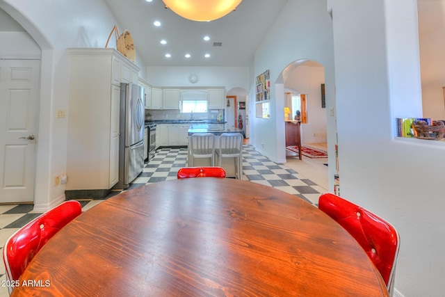 dining space featuring visible vents, light floors, recessed lighting, arched walkways, and high vaulted ceiling