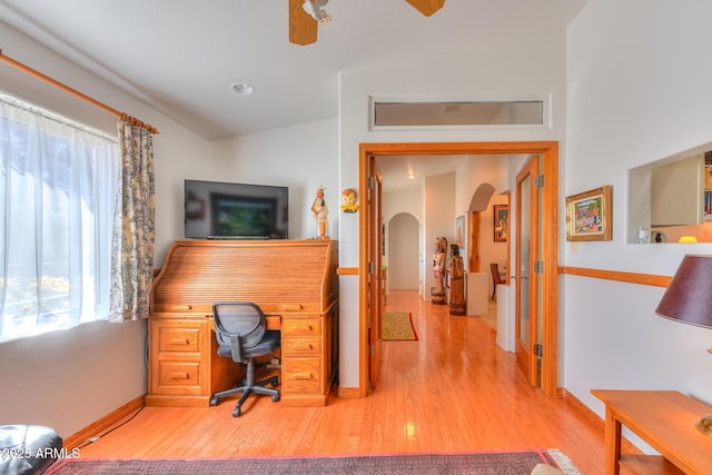 office area with baseboards, light wood-type flooring, lofted ceiling, arched walkways, and a ceiling fan