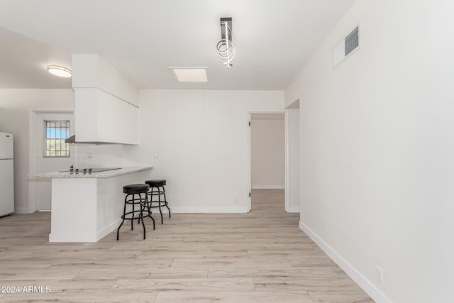 kitchen with white cabinetry, white refrigerator, kitchen peninsula, decorative light fixtures, and a breakfast bar