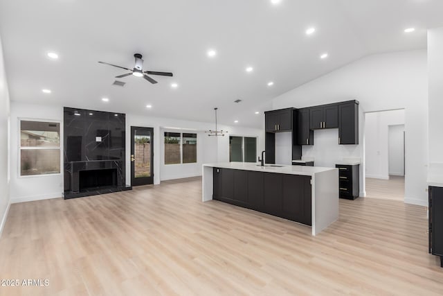 kitchen featuring light wood-type flooring, an island with sink, a ceiling fan, a sink, and a fireplace