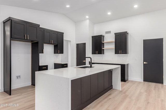 kitchen with visible vents, a sink, an island with sink, light wood-style floors, and open shelves