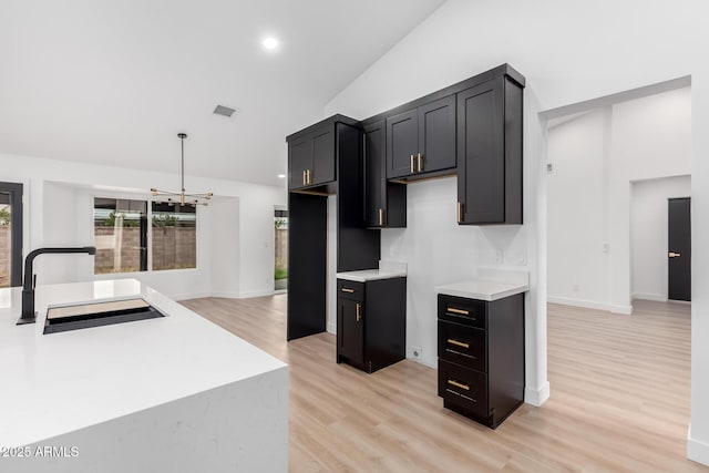 kitchen featuring light wood finished floors, vaulted ceiling, light countertops, and a sink