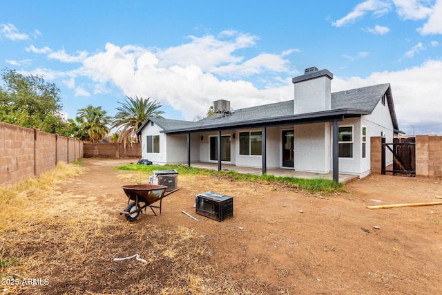 rear view of property with a fenced backyard, a fire pit, central AC unit, a chimney, and a patio area