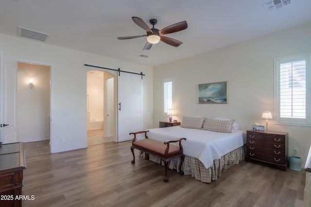 bedroom featuring ceiling fan, ensuite bath, wood-type flooring, and a barn door