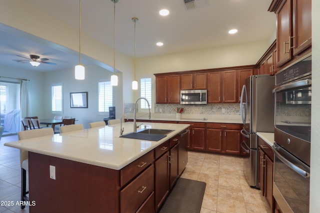 kitchen with sink, backsplash, stainless steel appliances, an island with sink, and a kitchen bar