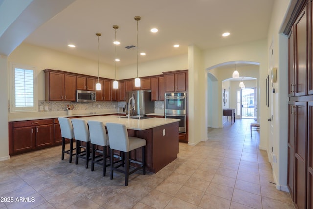 kitchen with a kitchen bar, hanging light fixtures, appliances with stainless steel finishes, a kitchen island with sink, and decorative backsplash