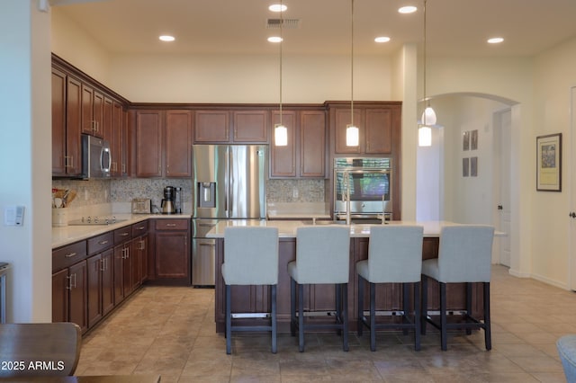 kitchen with tasteful backsplash, hanging light fixtures, stainless steel appliances, and an island with sink